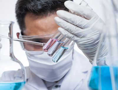 Ein Mann mit Mundschutz untersucht Flüssigkeit in einem Reagenzglas
