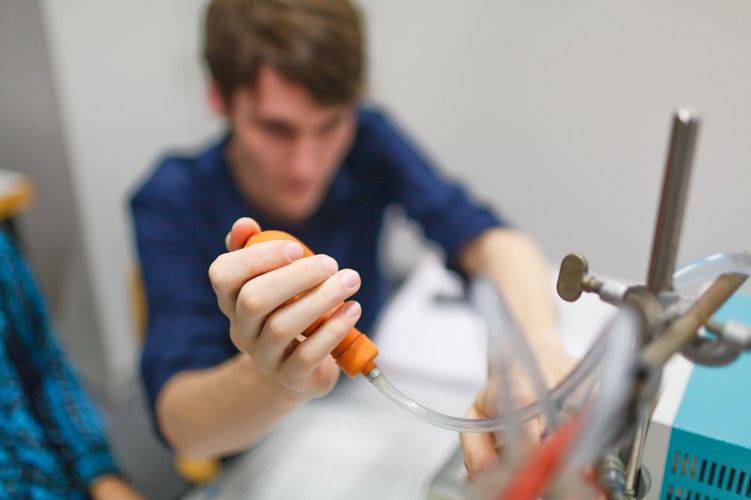 Student hält etwas in der Hand und arbeitet an einem Versuchsaufbau, Foto: Christian Hüller