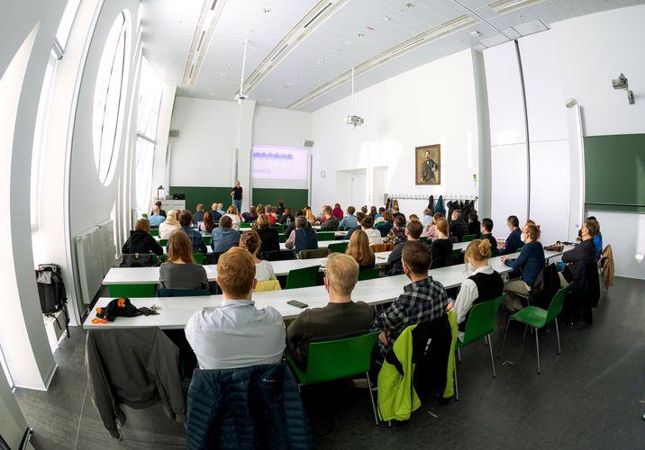 A lecture hall filled with people sitting and listening to a man standing in front of them