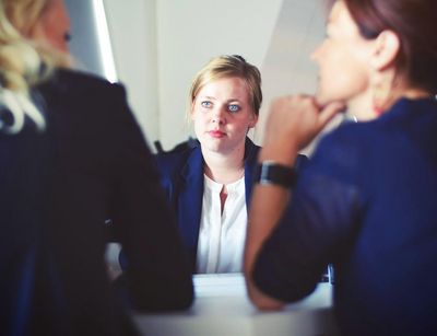 Foto: eine junge Frau sitzt in einer Gesprächssituation zwei anderen Frauen gegebüber