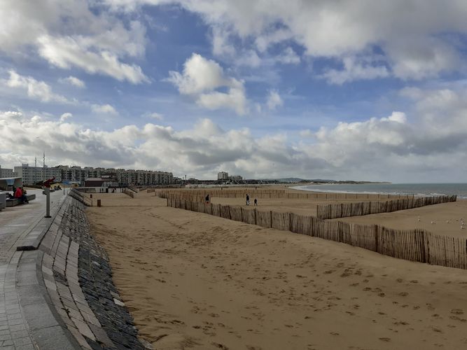 Farbfoto: Aufnahme eines breiten Strandes mit hölzernen Strandzäunen. Im Hintergrund befinden sich Häuser 