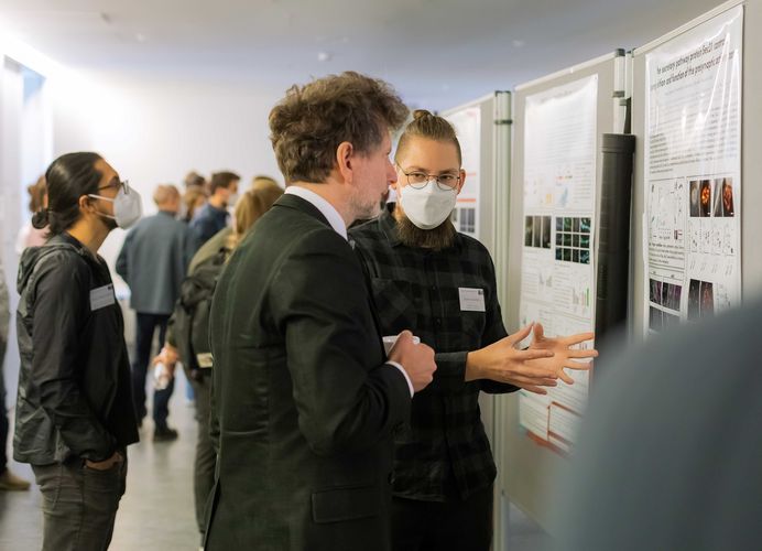 Two men standing and discussing in front of the poster