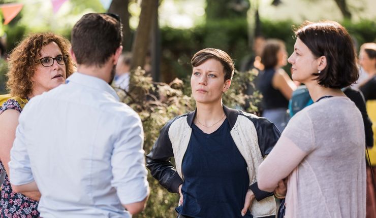 Farbfoto: Drei Frauen und ein Mann stehen im Freien zusammen und unterhalten sich. Die Atmosphäre im Bild ist locker und sommerlich
