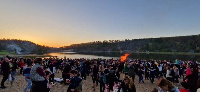 Viele Menschen stehen um ein Feuer in der Nähe eines Sees in der Abenddämmerung 