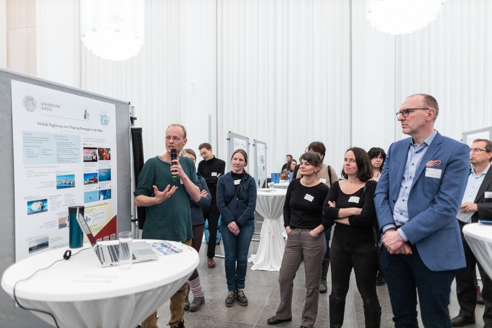 zur Vergrößerungsansicht des Bildes: Gruppe von Personen vor einem Plakat