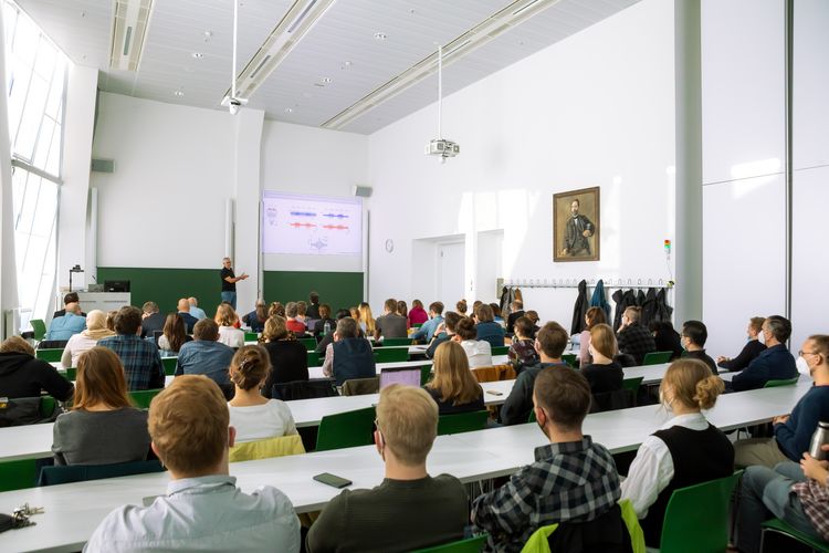 A professor explaining a presentation slide in front of the symposium participants in a lecture hall