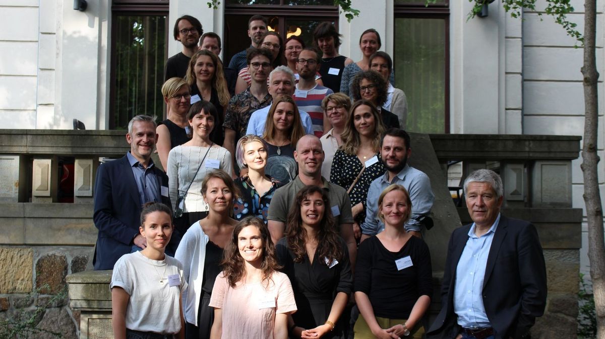 zur Vergrößerungsansicht des Bildes: Gruppenfoto vom Leipziger Arqus-Sommerfest 2022, Menschen auf einer Außentreppe verteilt stehend und in die Kamera lächelnd