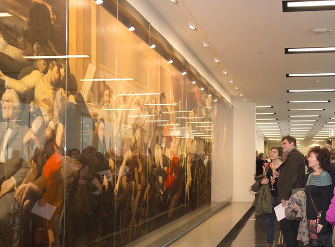 Links ist ein Teil des Wandgemäldes von Werner Tübke zu sehen, allerdings hinter einer Glasvitrine mit Spiegelungen. Davor und rechts im Bild stehen die Besucher der Veranstaltung, die über das Bild diskutieren.