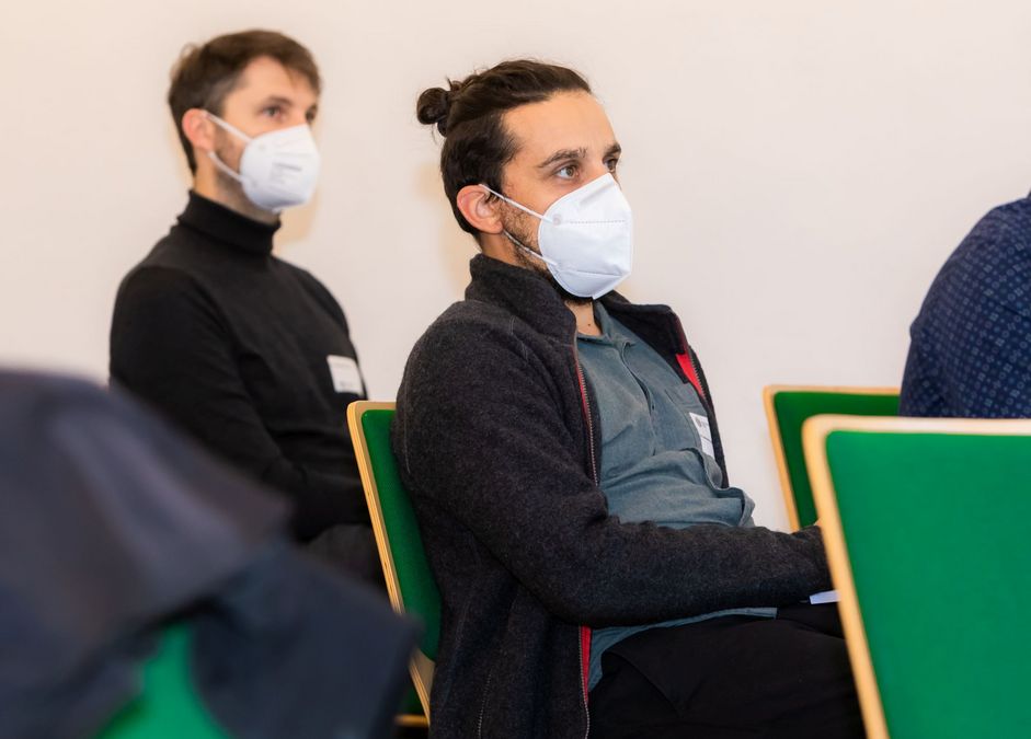 zur Vergrößerungsansicht des Bildes: Zwei Teilnehmende des Pre-Doc Awards sitzen im Publikum und hören offenbar aufmerksam zu.
