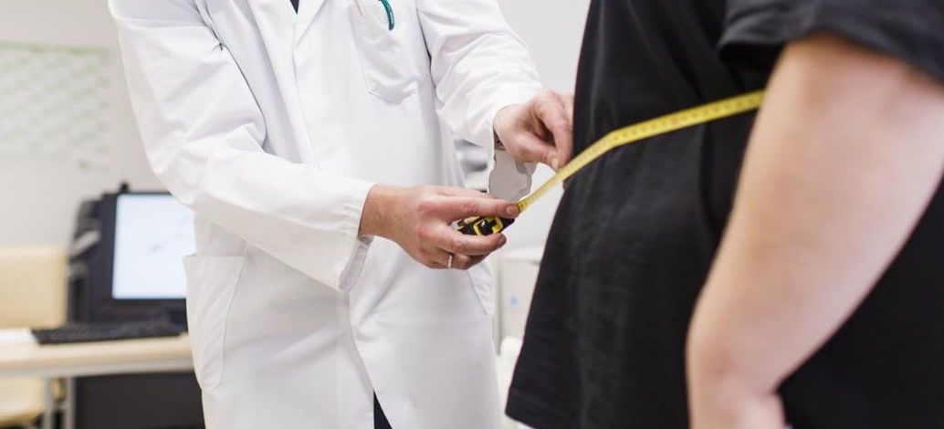 Foto: ein Arzt misst mit einem Maßband den Umfang des Bauches einer Frau