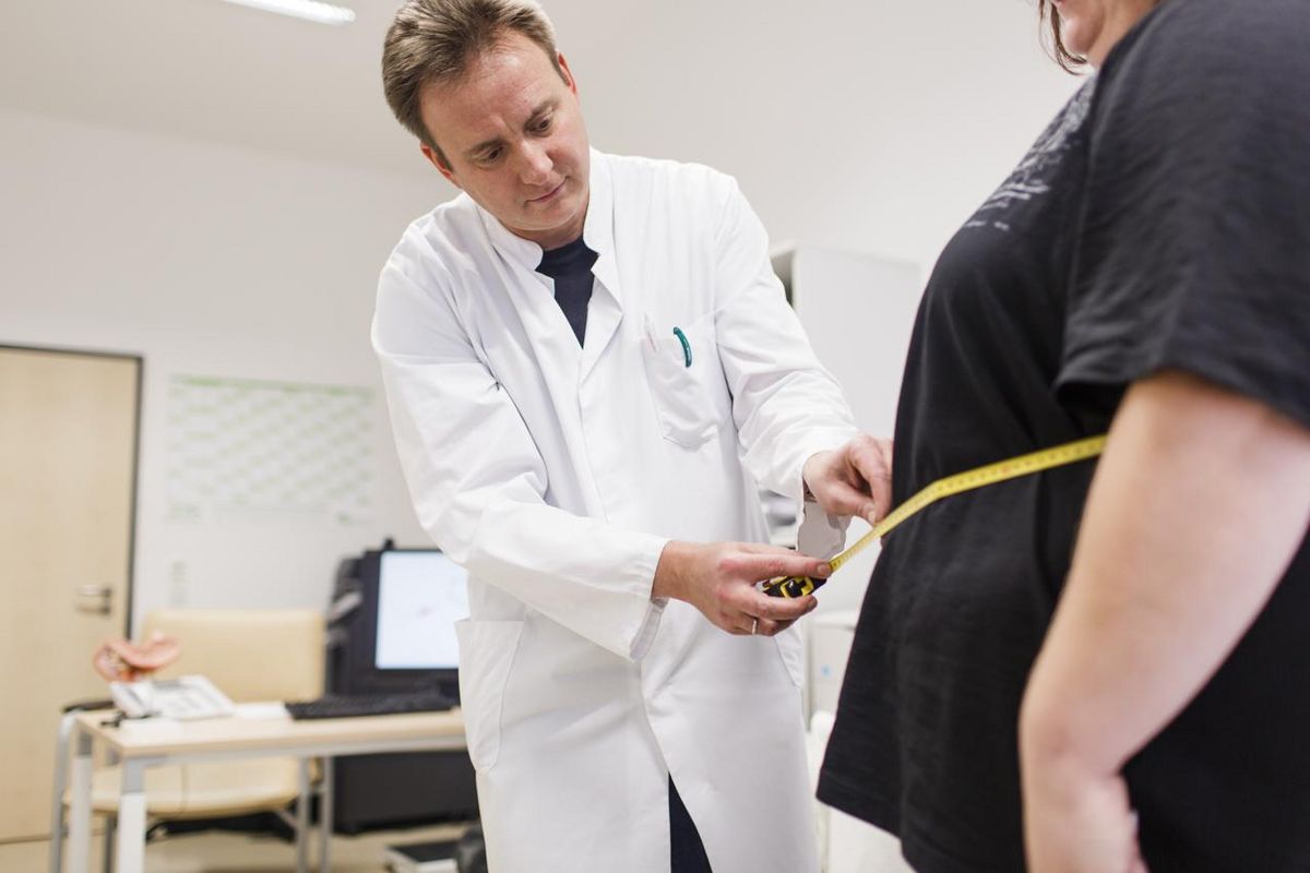 Foto: ein Arzt misst mit einem Maßband den Umfang des Bauches einer Frau