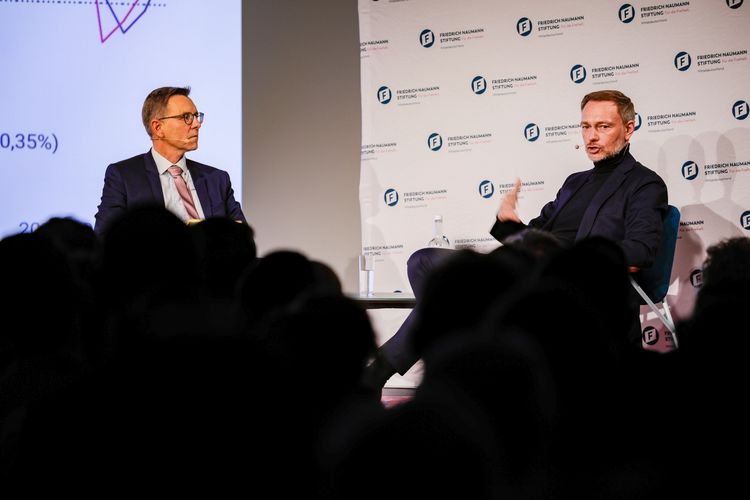 Prof. Dr. Gunther Schnabl (links) sitzend auf der Bühne zusammen mit Bundesfinanzminister Christian Lindner.