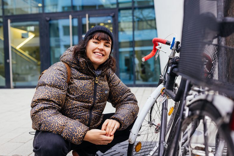 Studienbotschafterin Leni hockt neben einem Fahrrad auf dem Campus, Foto: Christian Hüller