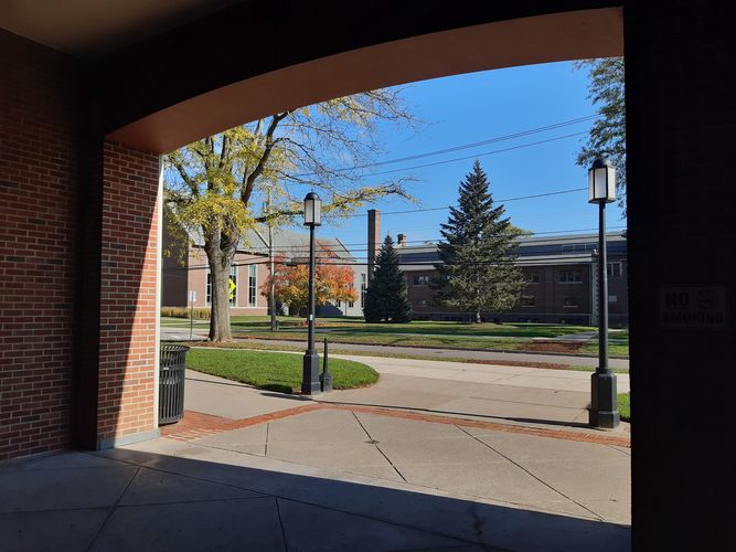 Das Bild ist aus einem Gebäudeeingang heraus fotografiert. Es ist ein Campus mit mehreren roten Backsteingebäuden zu sehen.
