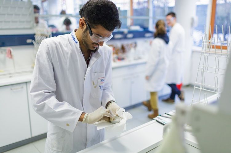 Studierende mit weißen Kitteln reinigen im Labor die Geräte, Foto: Christian Hüller