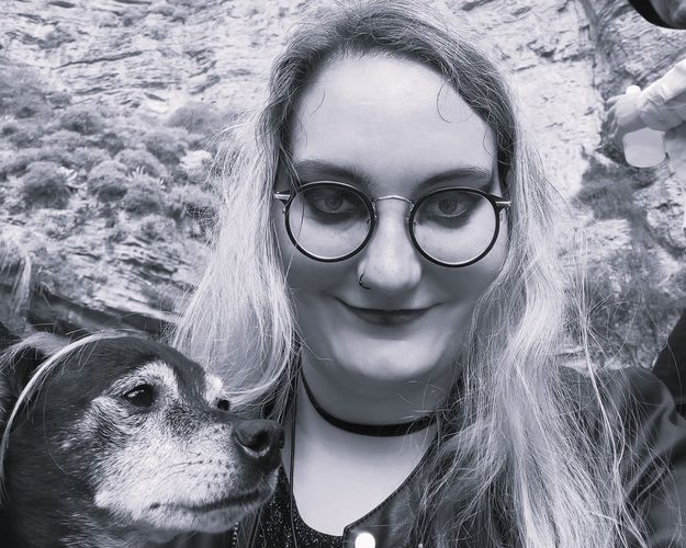 Gesicht einer blonden Person mit Brille, links davon ein Hund, in schwarz-weiß
