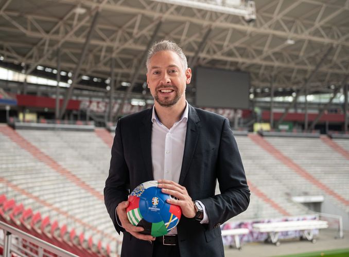 ZU sehen ist Stefan Schedler, der mit einem Fußball in der Hand im EM-Stadion steht.