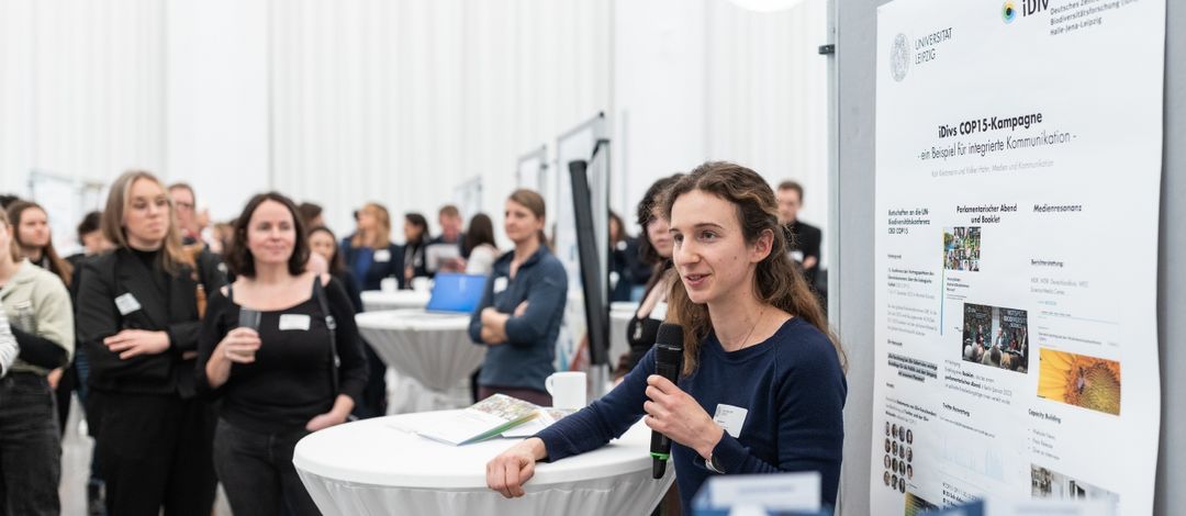 Katie Kietzmann erklärt mit einem Mikro etwas vor einem Plakat.