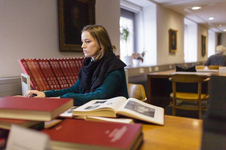 Studentin arbeitet am Computer und um ihr liegen viele Bücher, die teilweise aufgeschlagen sind, Foto: Christian Hüller