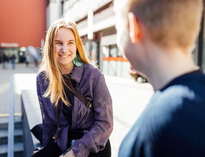 Studienbotschafterin Natalie lächelt beim Gespräch auf dem Campus, die Sonne scheint im Hintergrund, Foto: Christian Hüller