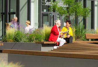 Teiknehmer:innen der Wissenschaftlichen Weiterbildung auf dem Campus am Augustusplatz, auf einer Bank sitzend.
