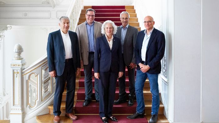 Farbfoto: Gruppenbild auf der Treppe im historischen Rektoratsgebäude. Im Mittelpunkt steht die Frau und rechts und links von ihr stehen je zwei Männer.