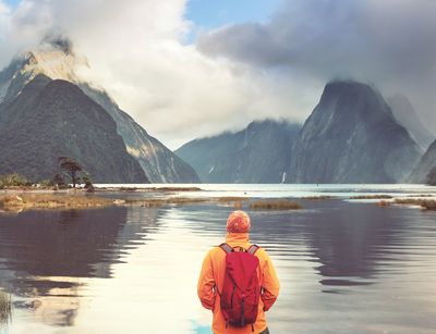 Mensch steht mit dem Rücken zur Kamera und schaut auf einen See und Berge