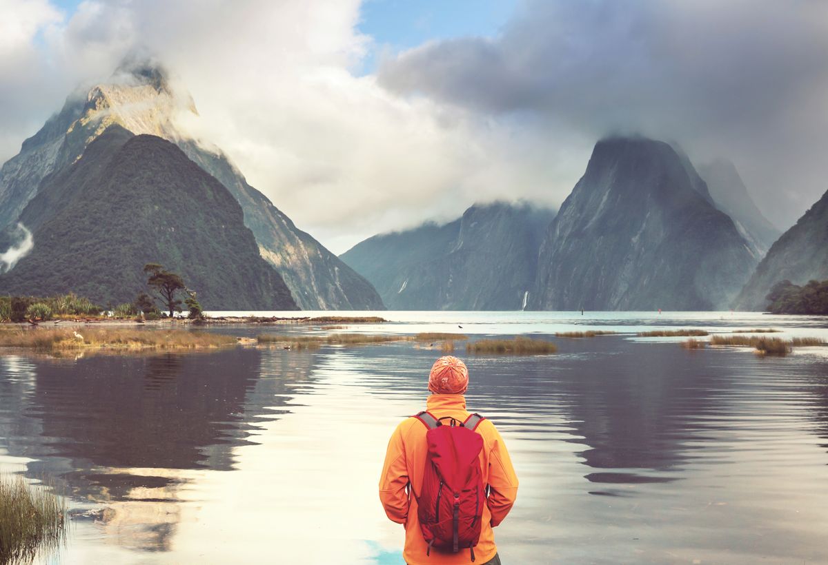 enlarge the image: Mensch steht mit dem Rücken zur Kamera und schaut auf einen See und Berge
