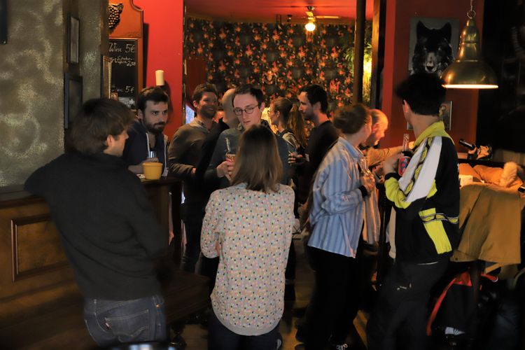 A group of people standing and talking in a cafe, some holding drinks.