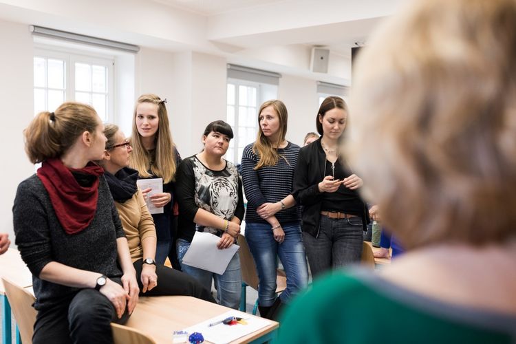 Man steht hinter der Dozentin und blickt auf Studierende die im Halbkreis vor ihr stehen. Zwei diskutieren gerade Ergebnisse, Foto: Christian Hüller