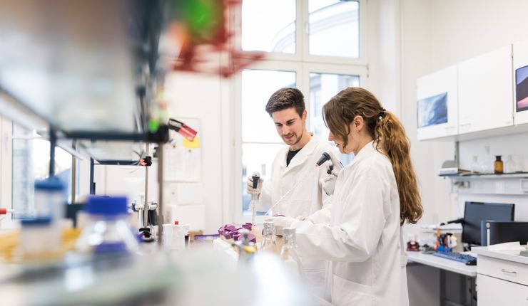 Farbfoto: Ein Mann und eine Frau stehen im Labor und arbeiten mit wissenschaftlichen Instrumenten.