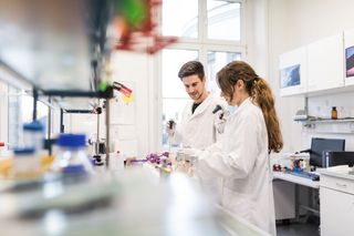 Farbfoto: Ein Mann und eine Frau stehen im Labor und arbeiten mit wissenschaftlichen Instrumenten.