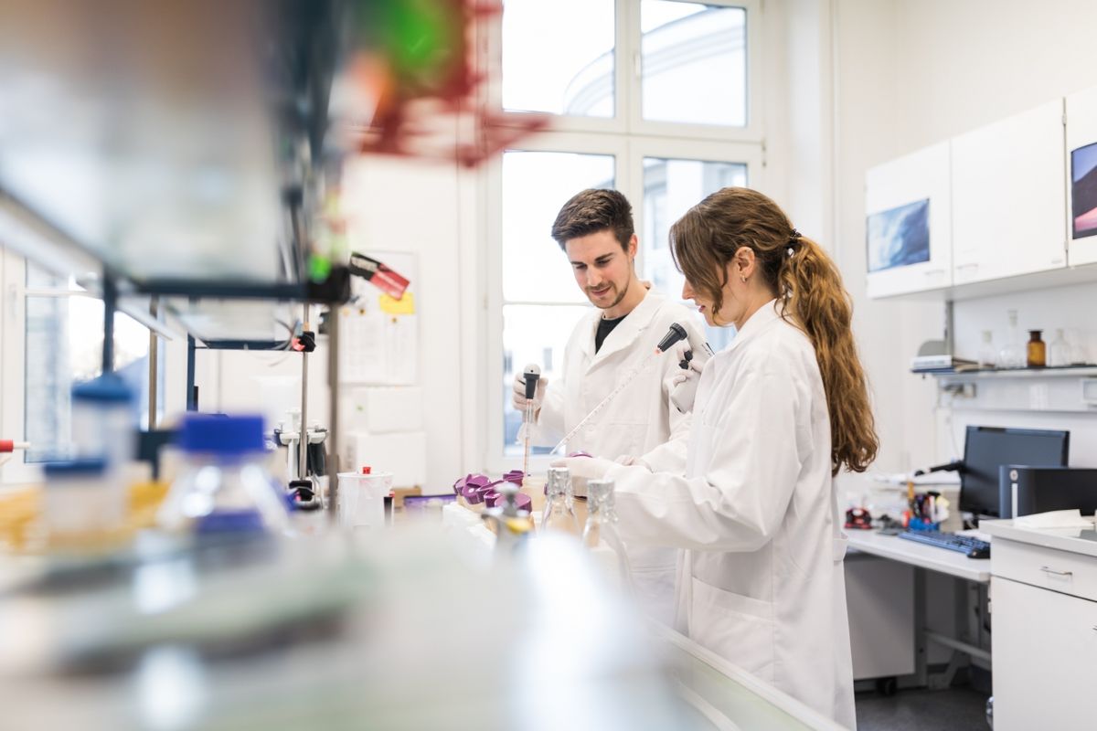 zur Vergrößerungsansicht des Bildes: Farbfoto: Ein Mann und eine Frau stehen im Labor und arbeiten mit wissenschaftlichen Instrumenten.