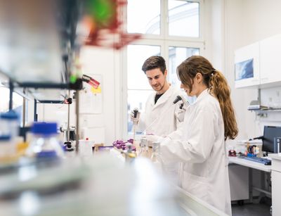 Farbfoto: Ein Mann und eine Frau stehen im Labor und arbeiten mit wissenschaftlichen Instrumenten.