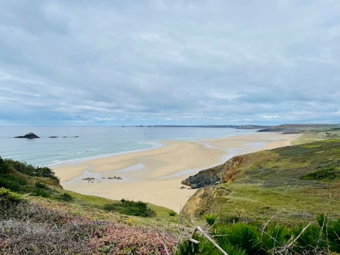 Zu sehen ist ein Strand in der Bildmitte. Dieser befindet sich tiefer als die Klippe, von der das Bild ausgenommen wurde. Im Hintergrund ist das Meer zu sehen.