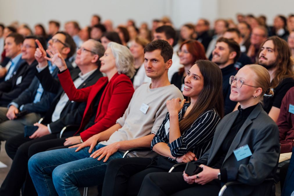 zur Vergrößerungsansicht des Bildes: Fördernde und Stipdentiaten sitzen in Reihen und schauen Richtung Bühne, einige Personen zeigen auf etwas, viele lachen
