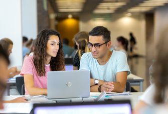 Student und Studentin schauen sich gemeinsam etwas auf einem Laptop an