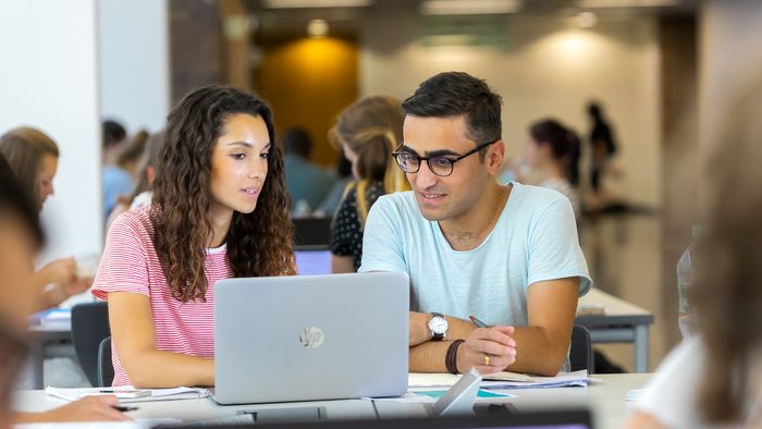 Student und Studentin schauen sich gemeinsam etwas auf einem Laptop an