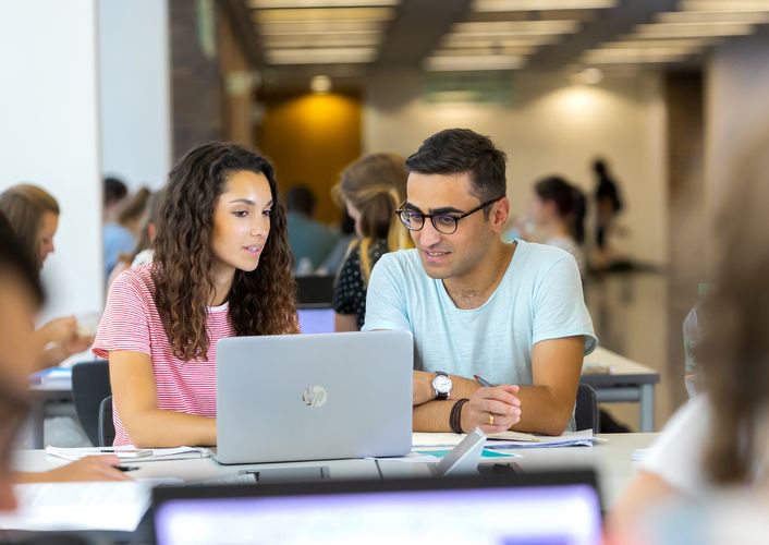 Student und Studentin schauen sich gemeinsam etwas auf einem Laptop an