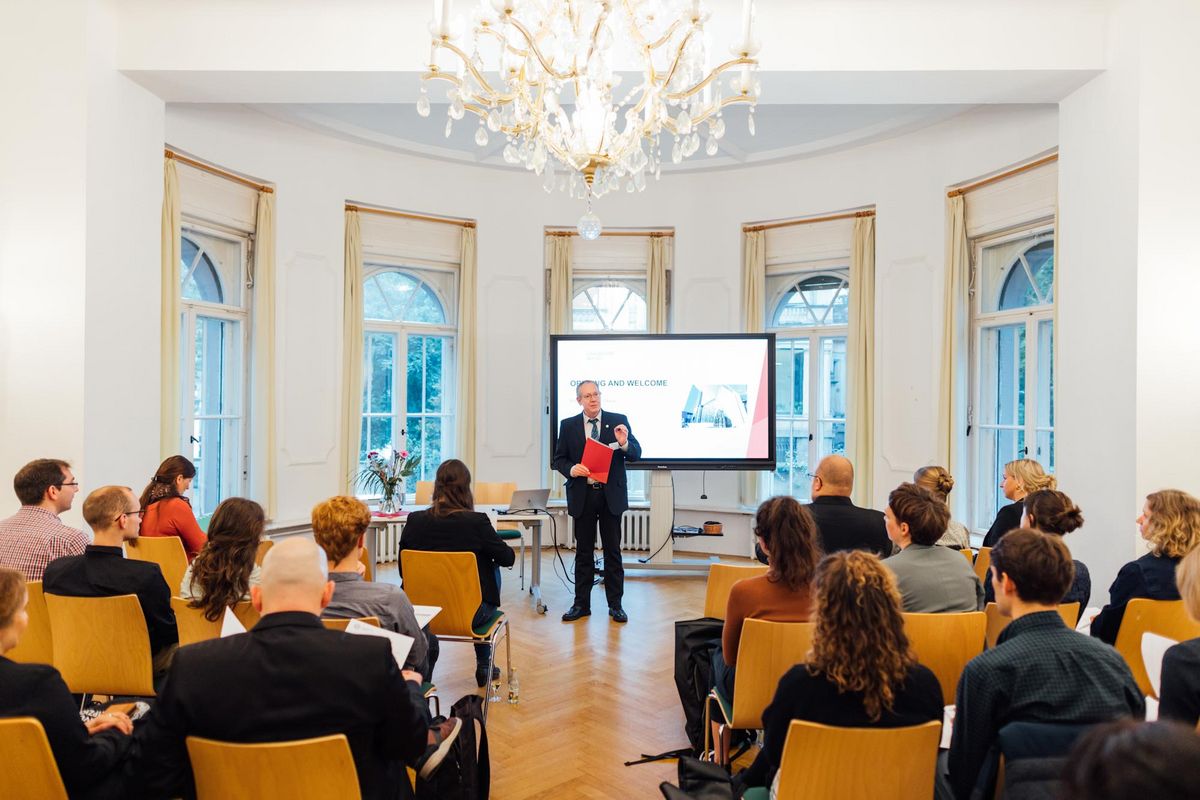 enlarge the image: A bright room with a lot of people sitting on chairs. At the front, Prorector Prof. Glaeser welcomes the new awardees to the Kick-Off event.