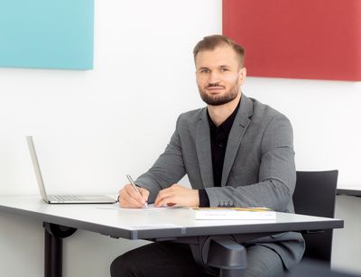 Farbfoto: Mann sitzt an einem Tisch und Blickt in die Kamera