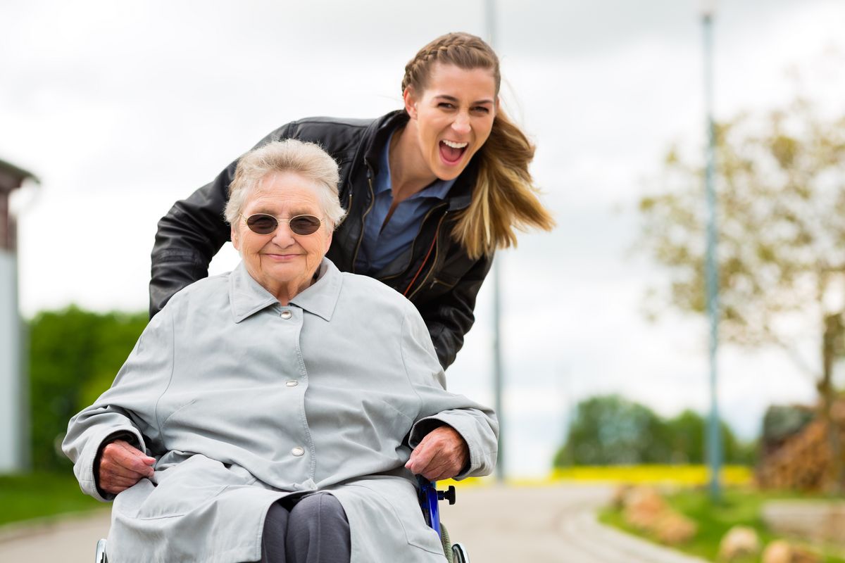Eine junge Frau schiebt eine ältere Dame in einem Rollstuhl, Foto: Colourbox