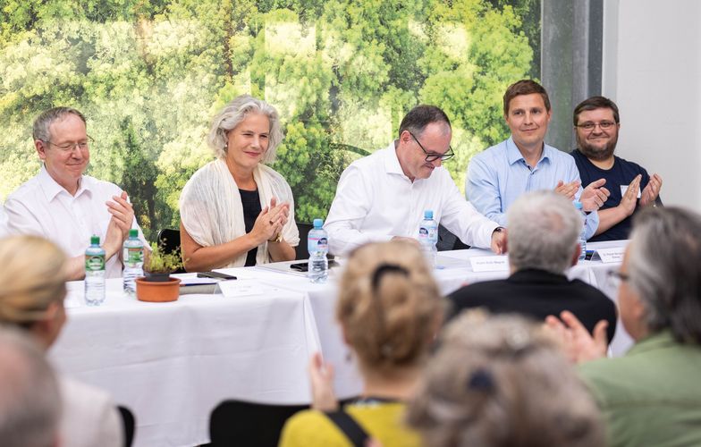 Foto mit Podium, zu sehen sind einige Vorstandsmitglieder und im Vordergrund von hinten einige Mitglieder der Universitätsgesellschaft.