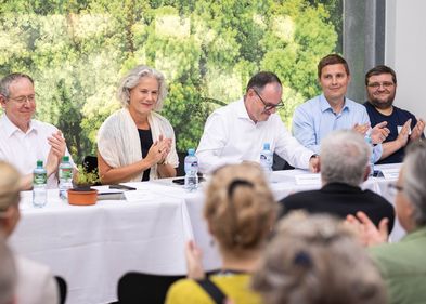 Foto mit Podium, zu sehen sind einige Vorstandsmitglieder und im Vordergrund von hinten einige Mitglieder der Universitätsgesellschaft.