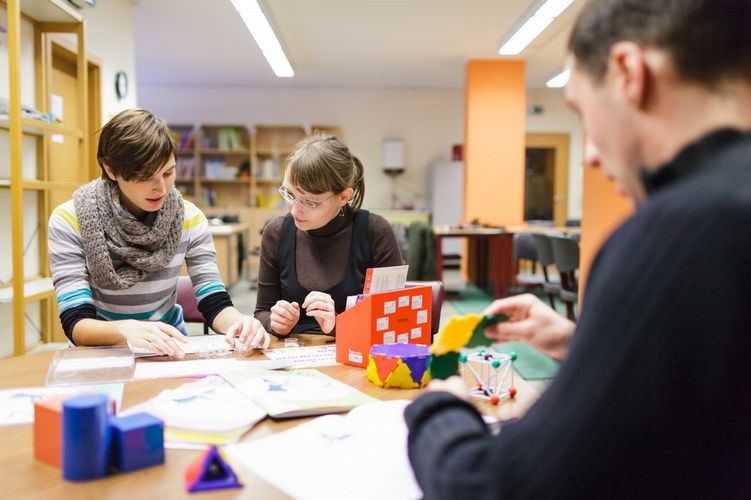 Drei Studierende sitzen zusammen an einem Tisch auf dem Arbeitsblätter und mathematische Modelle stehen, Foto: Christian Hüller