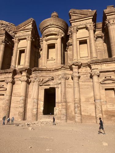 Das Foto zeigt die Frontansicht des Ad-Deir Kloster in Petra. Vor dem Kloster sieht man Menschen spazieren. 