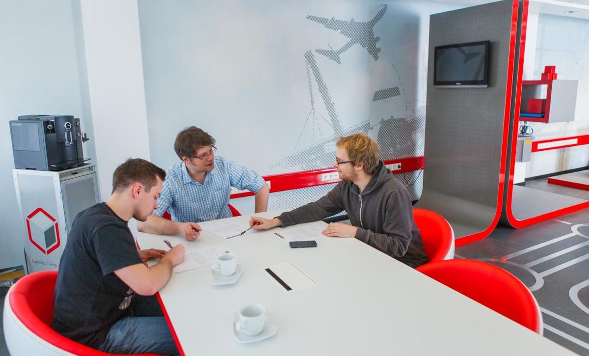 Foto: drei junge Männer sitzen an einem Tisch in einem modern eingerichteten Büro