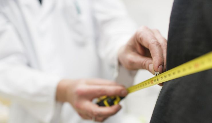 Foto: ein Arzt legt ein Maßband um den Körper eines Patienten