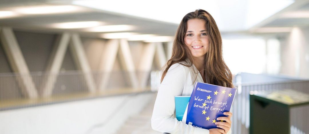 Junge Frau mit Erasmus Prospekten steht in der Uni