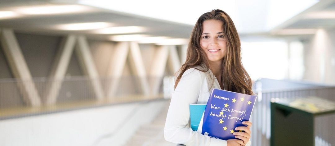 Junge Frau mit Erasmus Prospekten steht in der Uni
